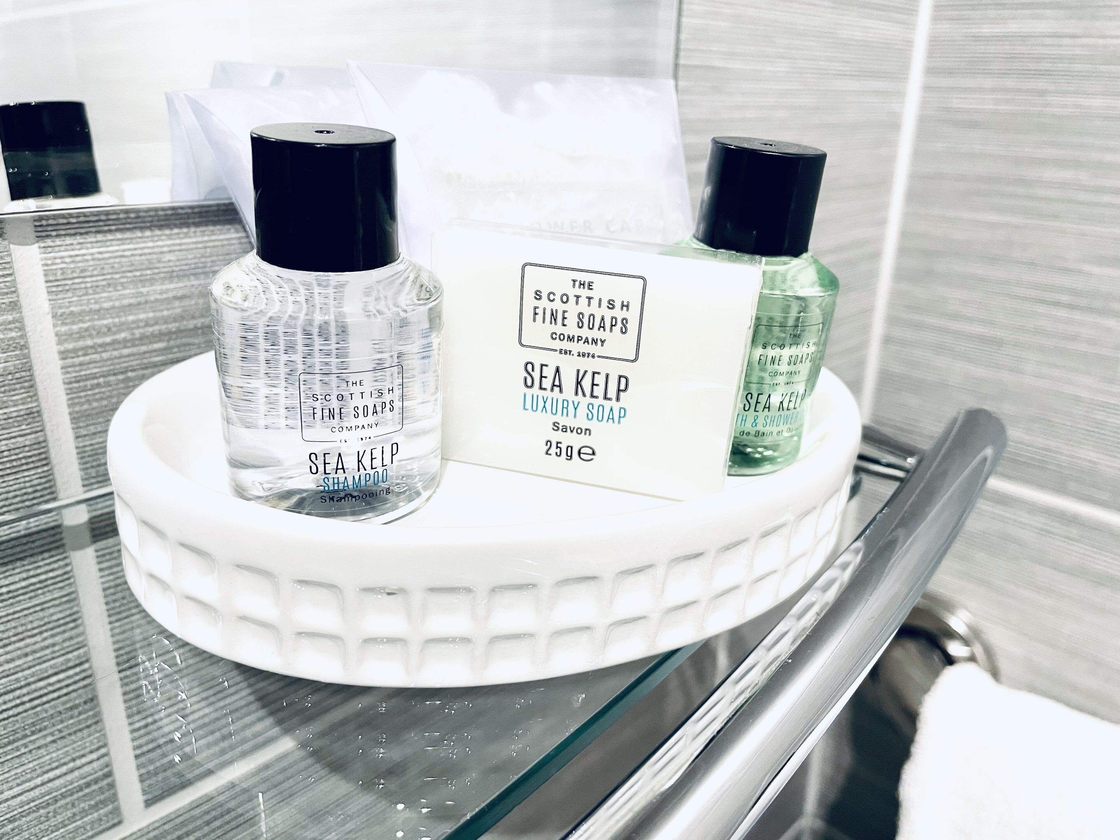 Une étagère de salle de bain avec trois bouteilles de shampoing à base d’algues marines, un savon de luxe aux algues marines et un gel douche aux algues marines.