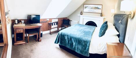 A bedroom with a bed, a desk, a chair, a television, a fireplace, and a framed picture on the wall.