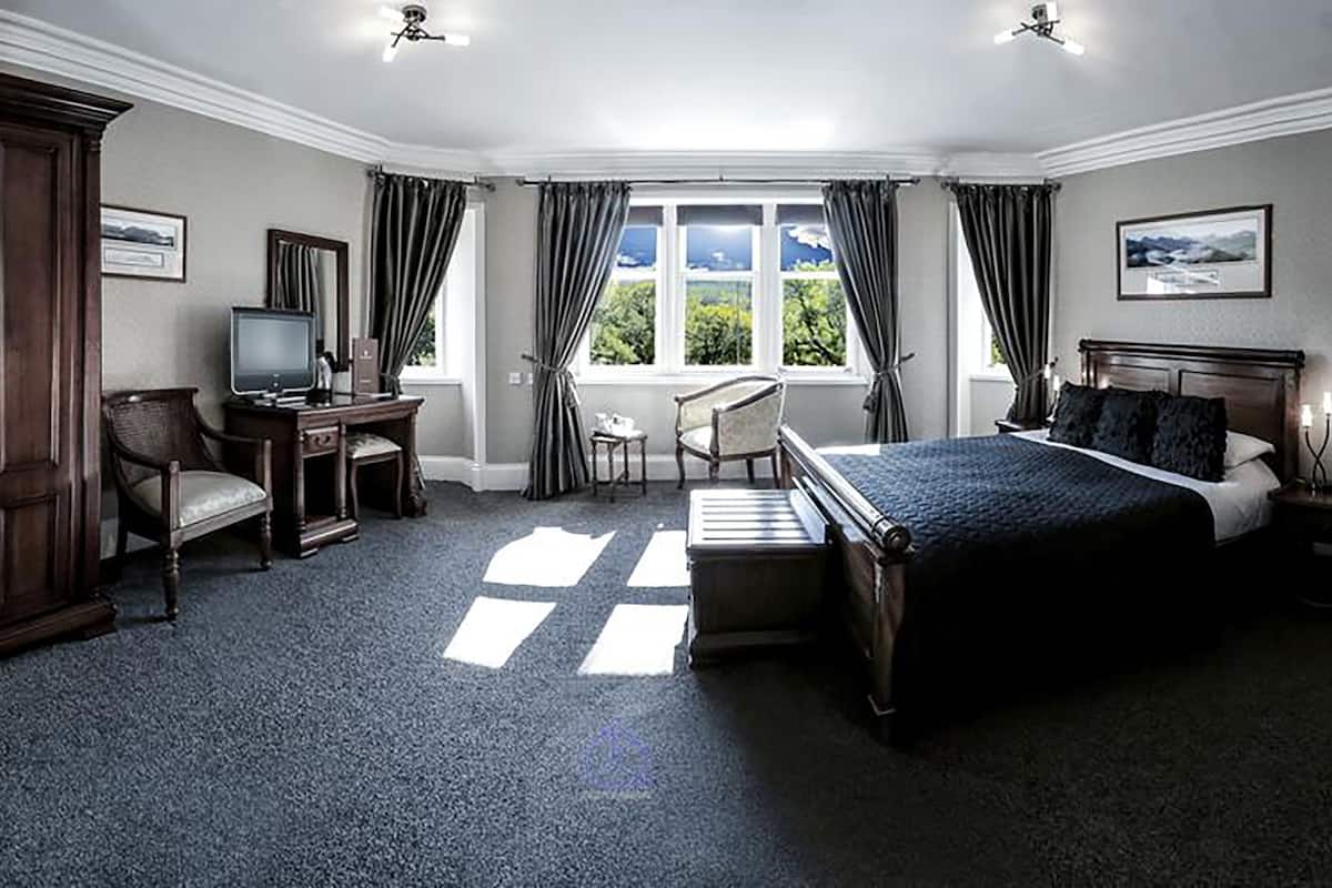A bedroom with a large bed, a desk with a computer, a chair, and a wardrobe.