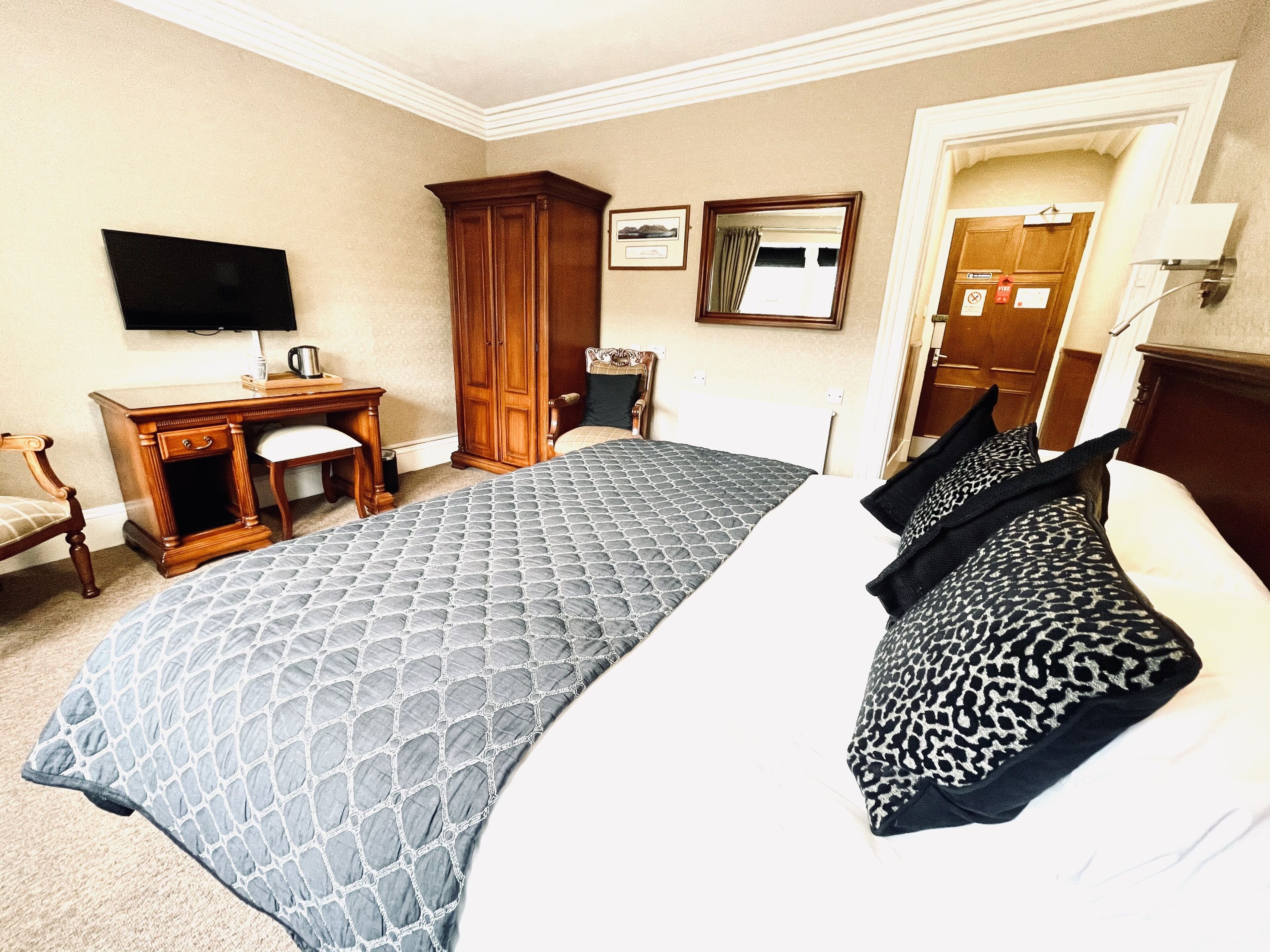 Ein Hotelzimmer mit einem großen Bett, einem Schreibtisch mit Stuhl, einem Kleiderschrank, einem Fernseher und einer Tür mit einem Hinweisschild.