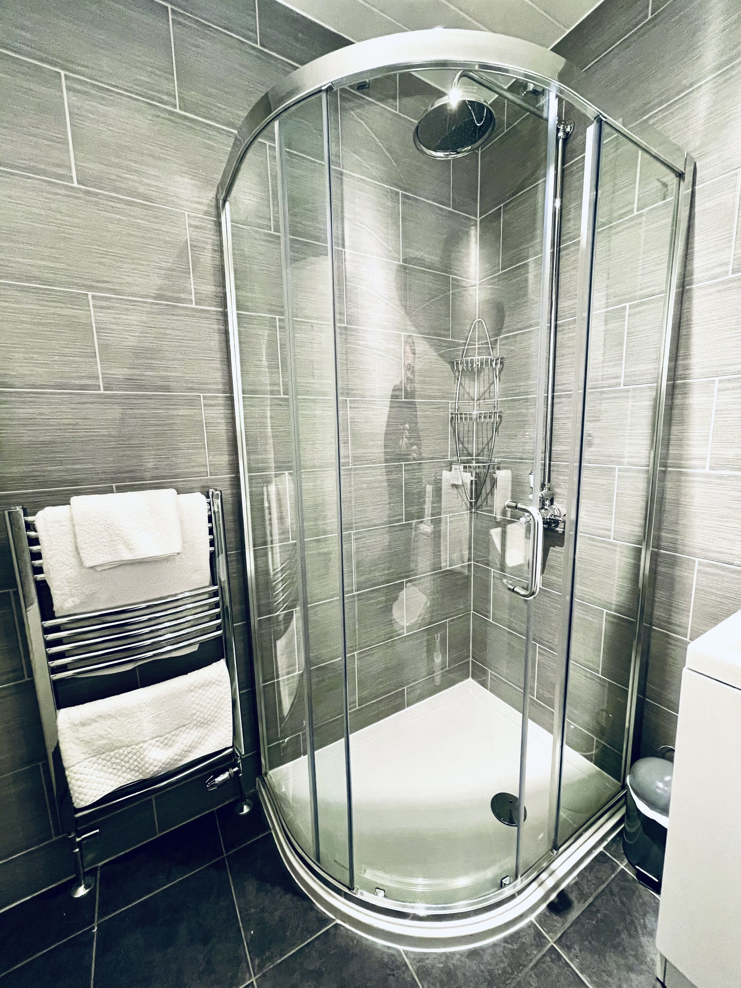 A modern bathroom with a glass-enclosed shower, a towel rack with white towels, and a toilet.