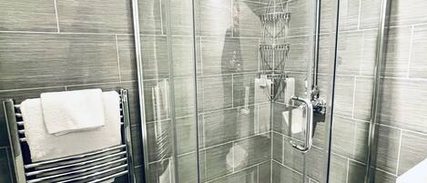 A modern bathroom with a glass-enclosed shower, a towel rack with white towels, and a toilet.