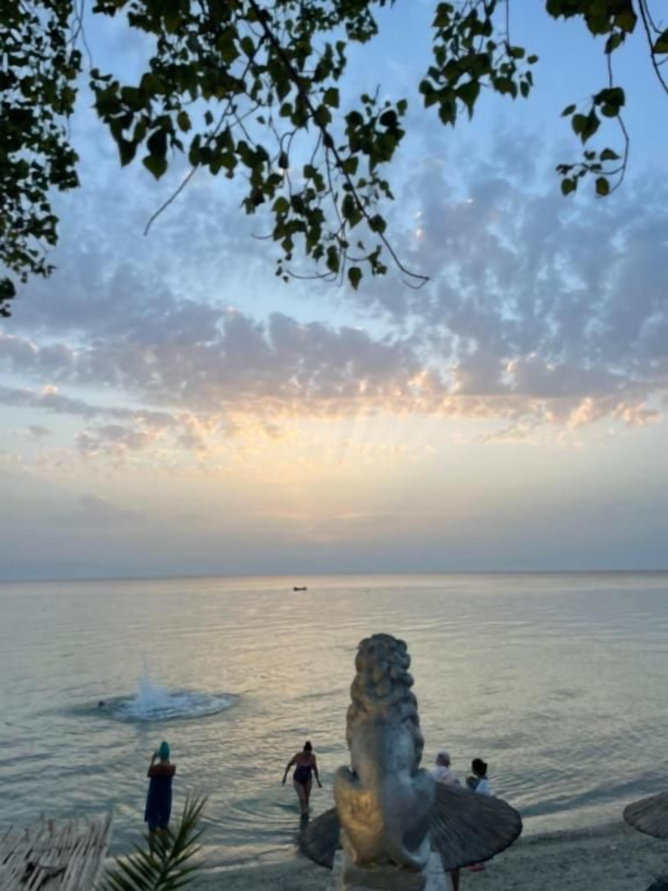 A beach scene with a statue, calm water, and a clear sky.