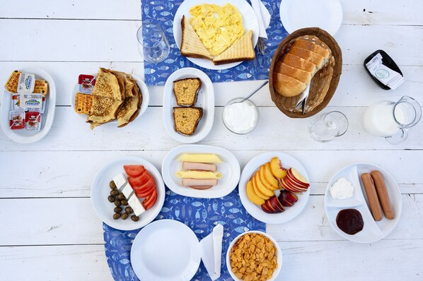 A table with various breakfast items including bread, eggs, sausages, and fruits.