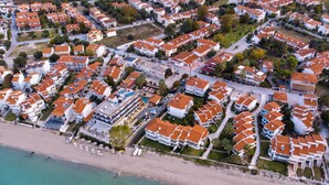 An aerial view of a coastal residential area with houses, a beach, and a clear sky. - Greek Pride Villa Ellada (Kassandra)