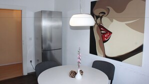 A modern dining area with a white table, two chairs, a white vase with flowers, a hanging light fixture, and a large abstract painting on the wall. - Ferienwohnung Fulda (Fulda)