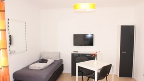 A compact room with a bed, a desk, a chair, a television, and a wardrobe. - Ferienwohnung Fulda (Fulda)