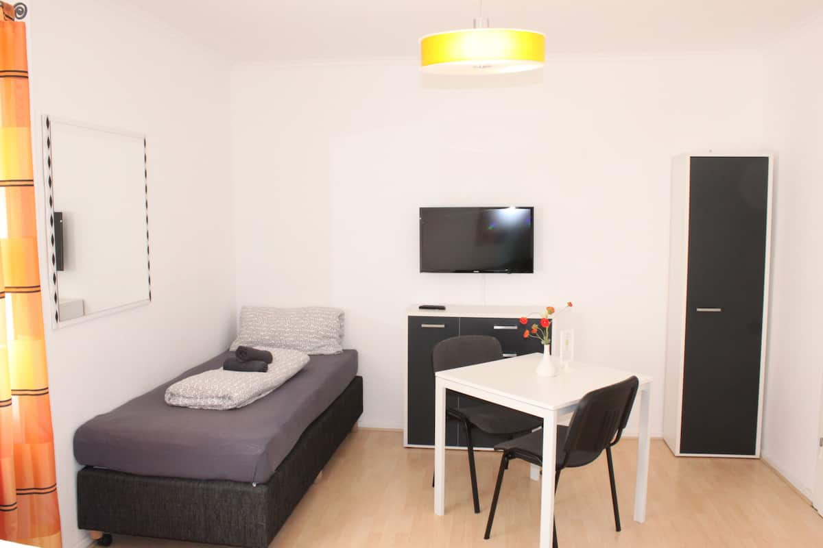 Una habitación compacta con cama, escritorio, silla, televisor y armario.
