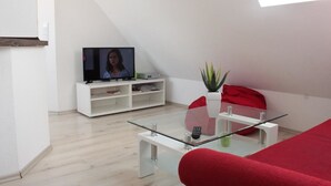 A modern living room with a glass coffee table, a red sofa, a white entertainment unit with a TV, and a potted plant. - Ferienwohnung Fulda (Fulda)