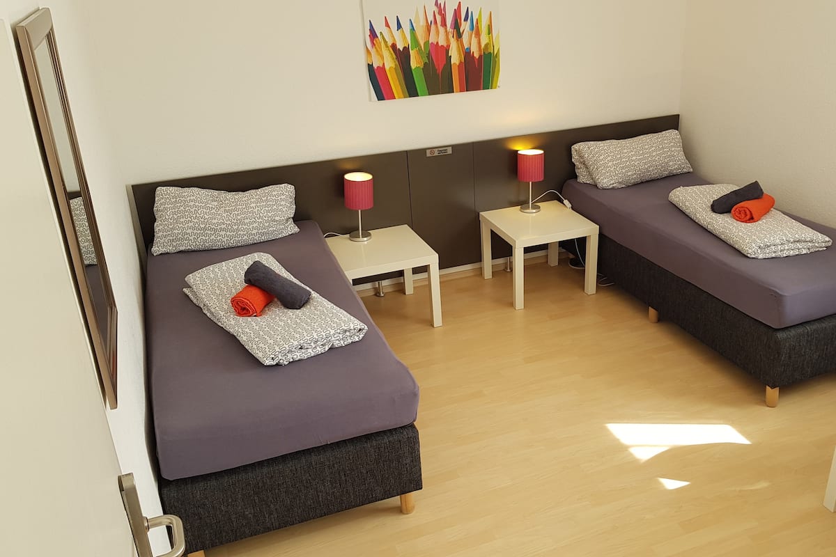 Una habitación de hotel compacta con dos camas, una mesita, un escritorio y una mesita de noche.