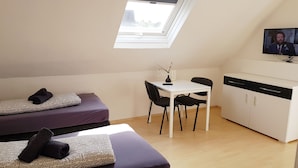 A small, modern room with a bed, a desk, a chair, and a television. - Ferienwohnung Fulda (Fulda)