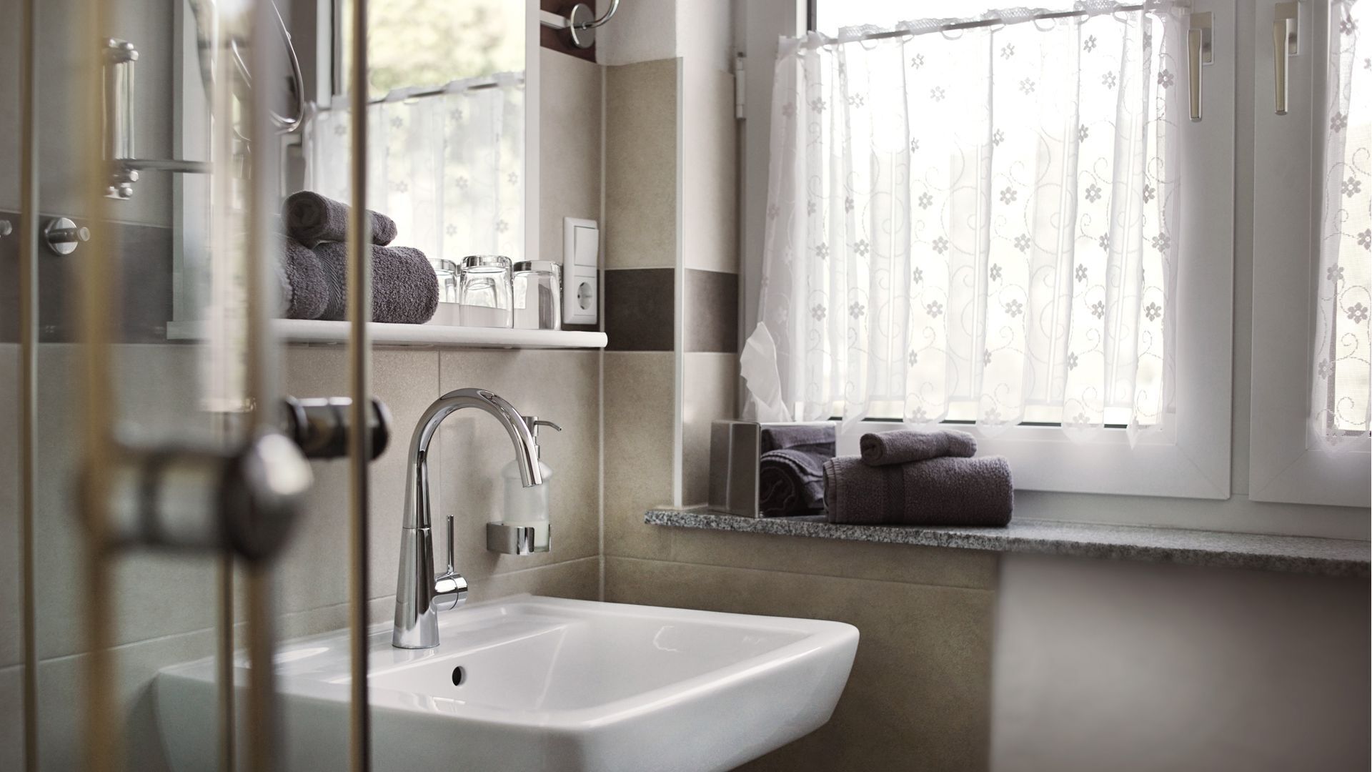 A bathroom with a white sink, chrome faucet, and a window with floral curtains.