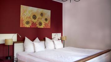 A hotel room with a large bed, white bedding, and a painting of sunflowers on the wall.
