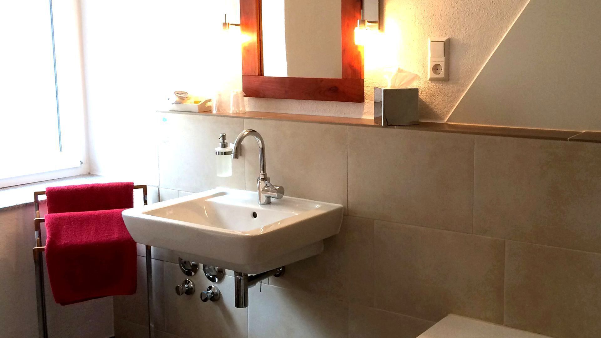 Ein Badezimmer mit einem weißen Waschbecken, einem roten Handtuch und einem Spiegel über dem Waschbecken.