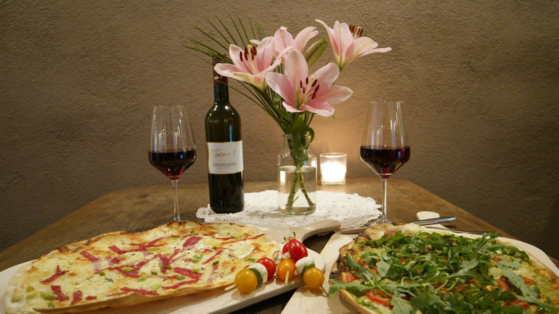 Une table avec deux pizzas, une bouteille de vin et un vase rempli de fleurs.