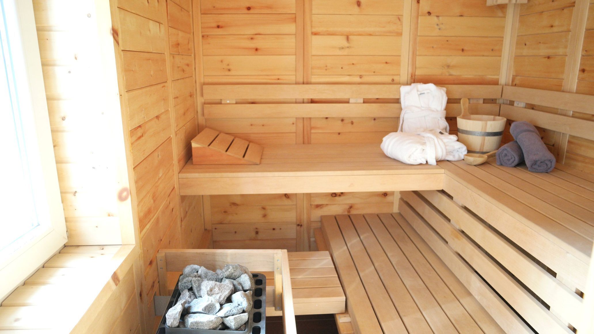 Een houten sauna met banken, een bank met een handdoek en een bak met stenen.