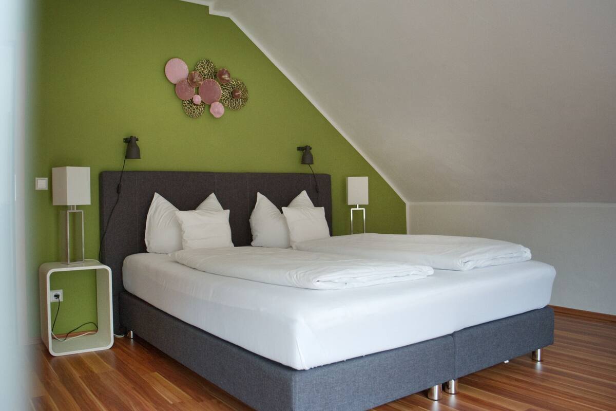 Ein modernes Schlafzimmer mit einem großen Bett, grünen Wänden und einer geneigten Decke.