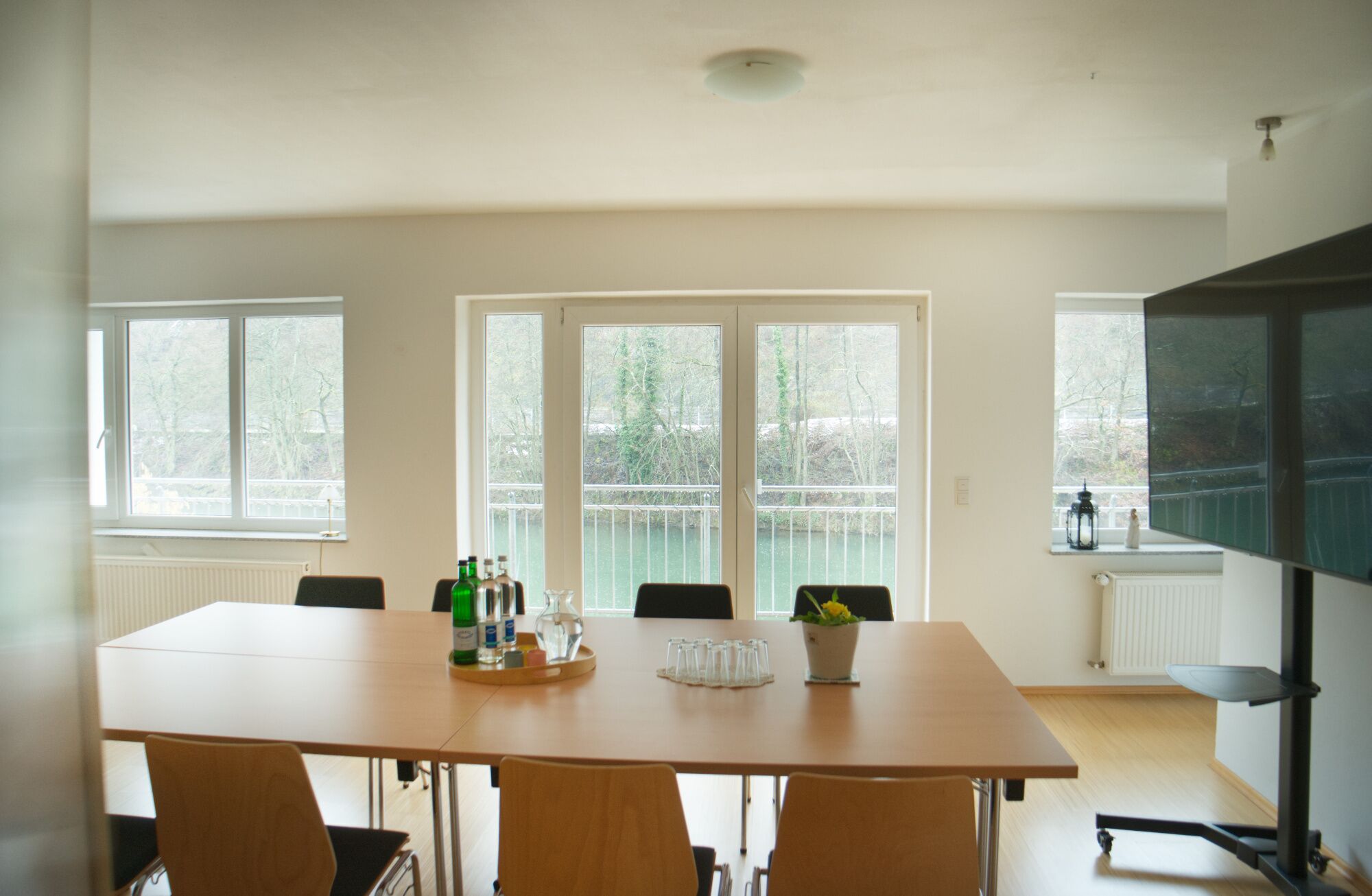 Une salle de conférence dotée d’une grande table, de chaises et de fenêtres offrant une vue sur les arbres et une rambarde.