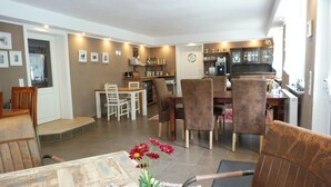 Un coin repas avec une table et des chaises en bois, une cuisine en arrière-plan et un petit arrangement floral sur la table.