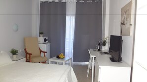 A bedroom with a bed, a desk with a laptop, a chair, a small table with fruits, and a potted plant. - Hotel Carlos I (Torremolinos)