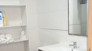 A bathroom with a white toilet, a wooden vanity with a sink, and a mirror above the sink. There are shelves with toiletries and a green trash bin. - Hotel Carlos I (Torremolinos)