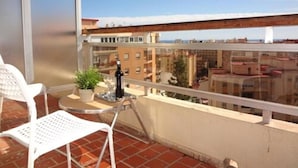 A balcony with a white chair, a small table, a potted plant, and a bottle. The view includes a cityscape with buildings and a clear sky. - Hotel Carlos I (Torremolinos)