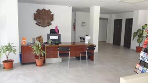 A reception area with a wooden desk, two chairs, a potted plant, and a coat rack. - Hotel Carlos I (Torremolinos)