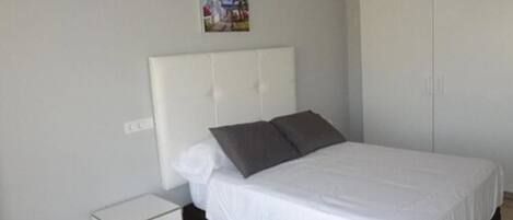 A bedroom with a white bed, two pillows, a nightstand, and a wardrobe.