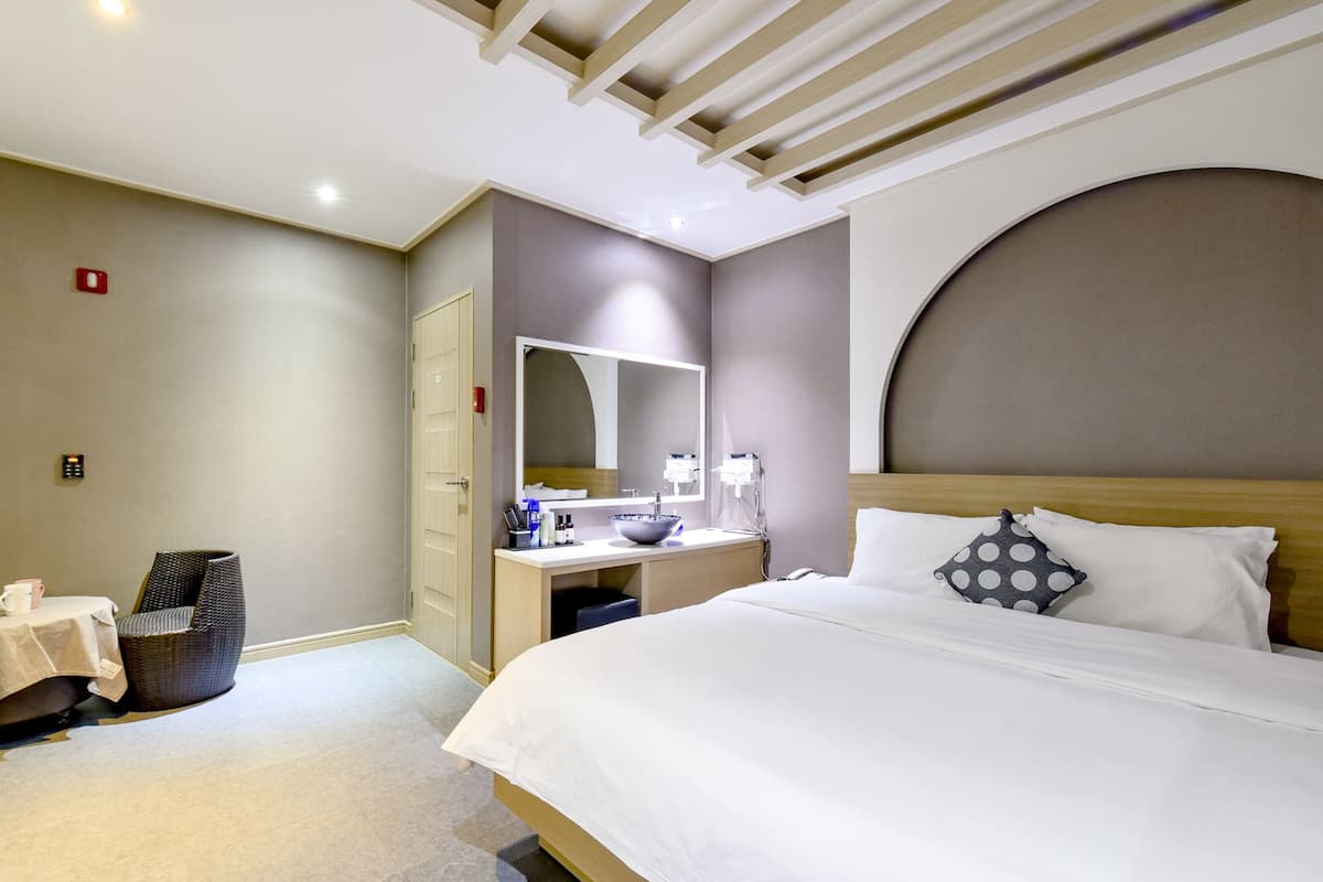 Habitación de hotel con una cama, un escritorio con espejo, una silla y una mesita con una taza.
