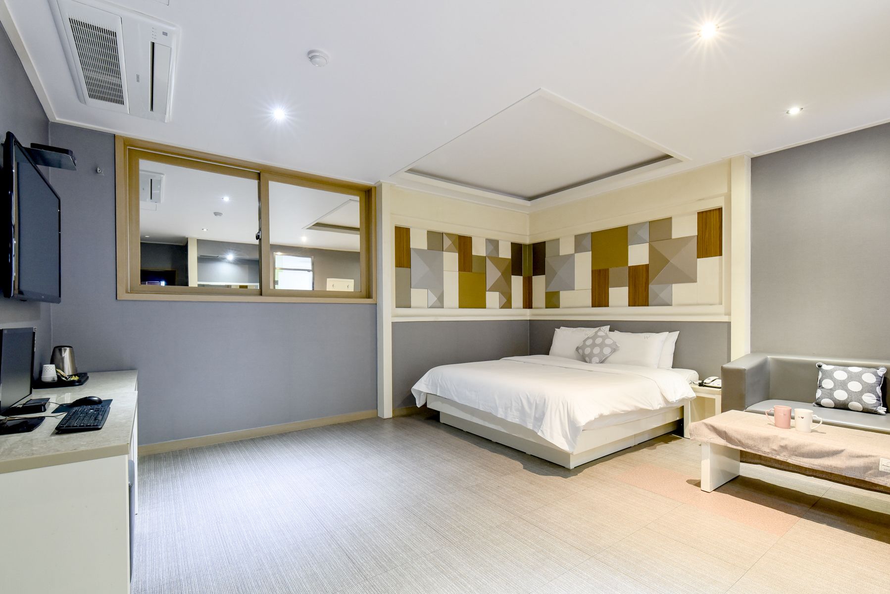 Una habitación de hotel moderna con cama, mesita de noche y escritorio con computadora.