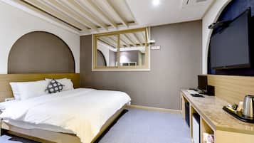 A hotel room with a bed, a desk with a computer, a mirror, and a TV.