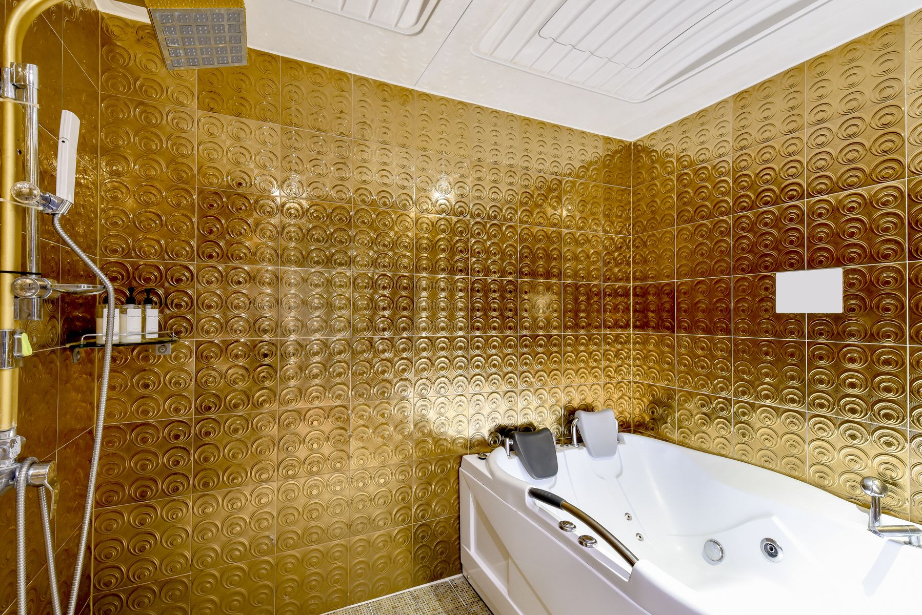A luxurious bathroom with a gold-tiled wall, a white bathtub, and a shower area with chrome fixtures.