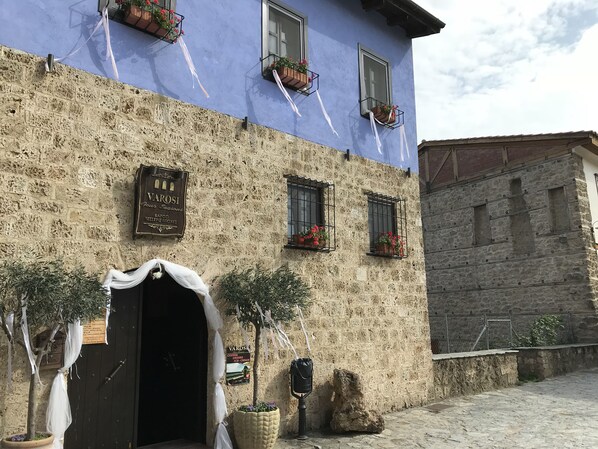 A building with a stone facade, multiple windows with flower boxes, and a sign indicating it is a tavern. - Varosi 4 Seasons (Edessa)