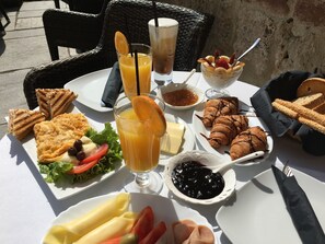 A table set with a variety of food items including sandwiches, croissants, and a bowl of fruit. - Varosi 4 Seasons (Edessa)