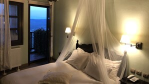 A bedroom with a bed, a bedside table with a phone, and a view of the outdoors. - Varosi 4 Seasons (Edessa)