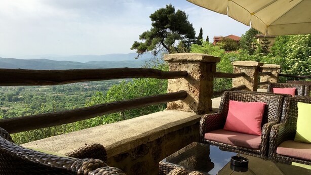A wicker outdoor seating area with a stone table and a view of a green landscape. - Varosi 4 Seasons (Edessa)