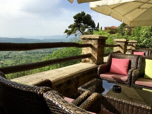 Un'area relax esterna con sedute in vimini, un tavolo in pietra e vista su un paesaggio verde.