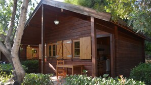 A wooden cabin with a porch, a table, and a chair. - Bungalows Los Pedregales (Estepona)
