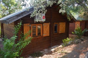 Una cabaña de madera con un porche pequeño, un aire acondicionado colgante y una puerta de madera.