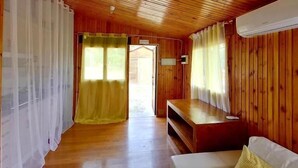 A wooden interior with a white sofa, a TV stand, and a door leading outside. - Bungalows Los Pedregales (Estepona)