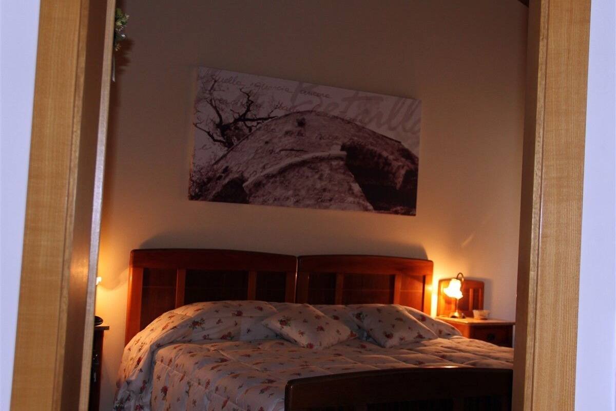A bedroom with a wooden bed, floral bedding, a nightstand with a lamp, and a wall-mounted picture.