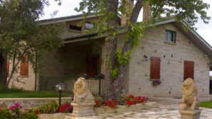 A stone building with a stone staircase leading to a porch, surrounded by flowering plants and two stone lion statues. - Villa Giardino degli Eventi (Fano)