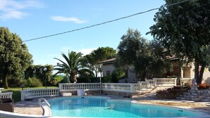 A pool with a white balustrade, surrounded by a stone patio and lush greenery. - Villa Giardino degli Eventi (Fano)