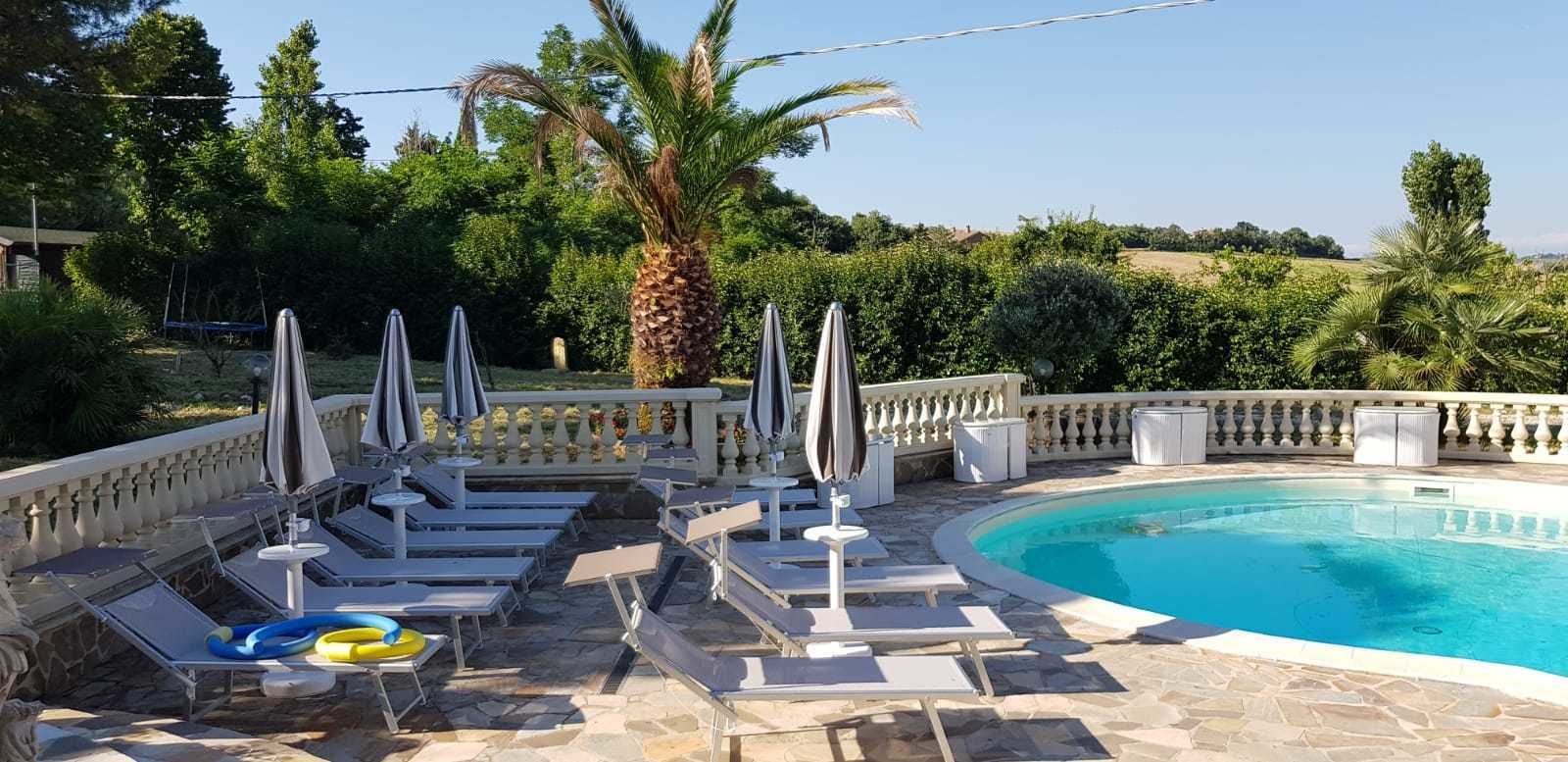 A poolside area with lounge chairs and umbrellas, surrounded by greenery and a clear blue pool.