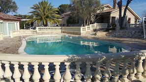 A swimming pool with a white balustrade, surrounded by stone steps and palm trees.
