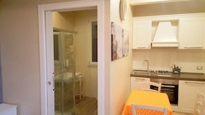 A compact kitchen with white cabinets, a gas stove, and a small dining table with an orange tablecloth.