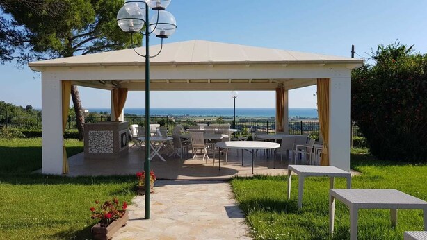 A covered outdoor seating area with a view of the sea, stone pillar, and outdoor furniture. - Villa Giardino degli Eventi (Fano)