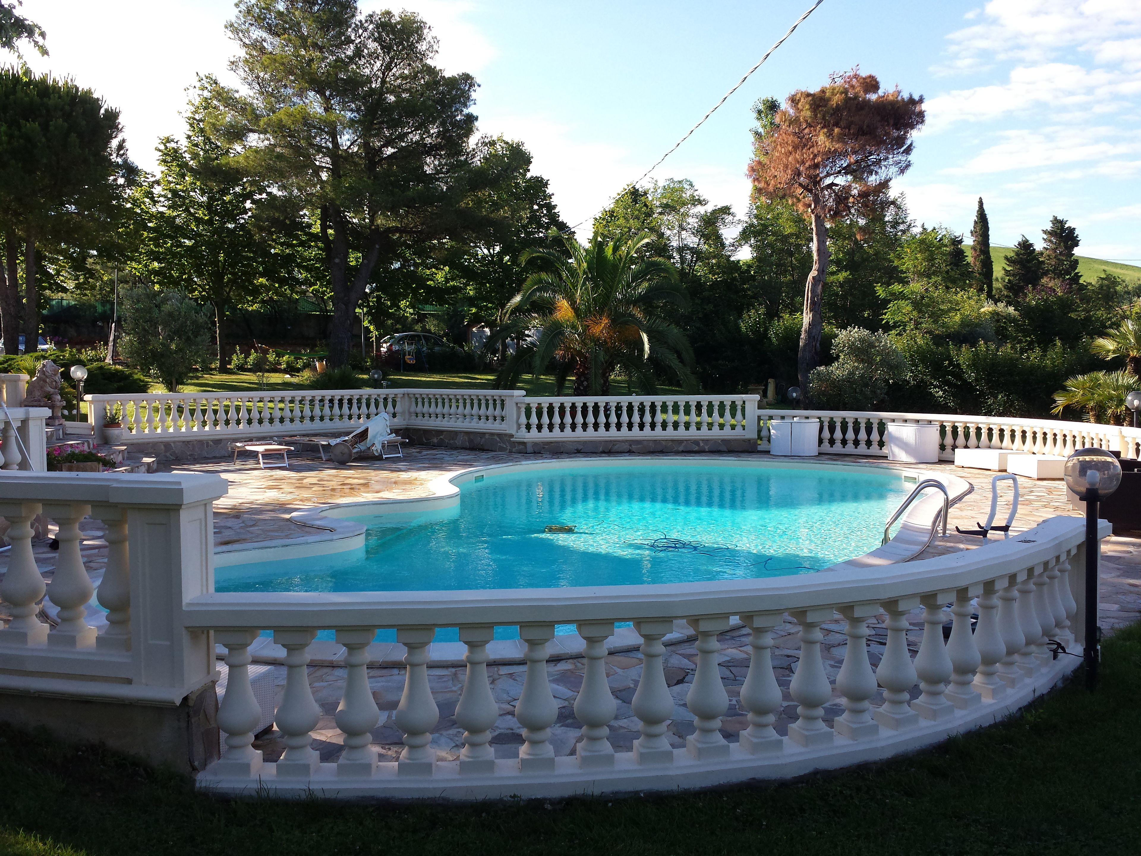Una piscina con barandilla blanca, rodeada de exuberante follaje y árboles.
