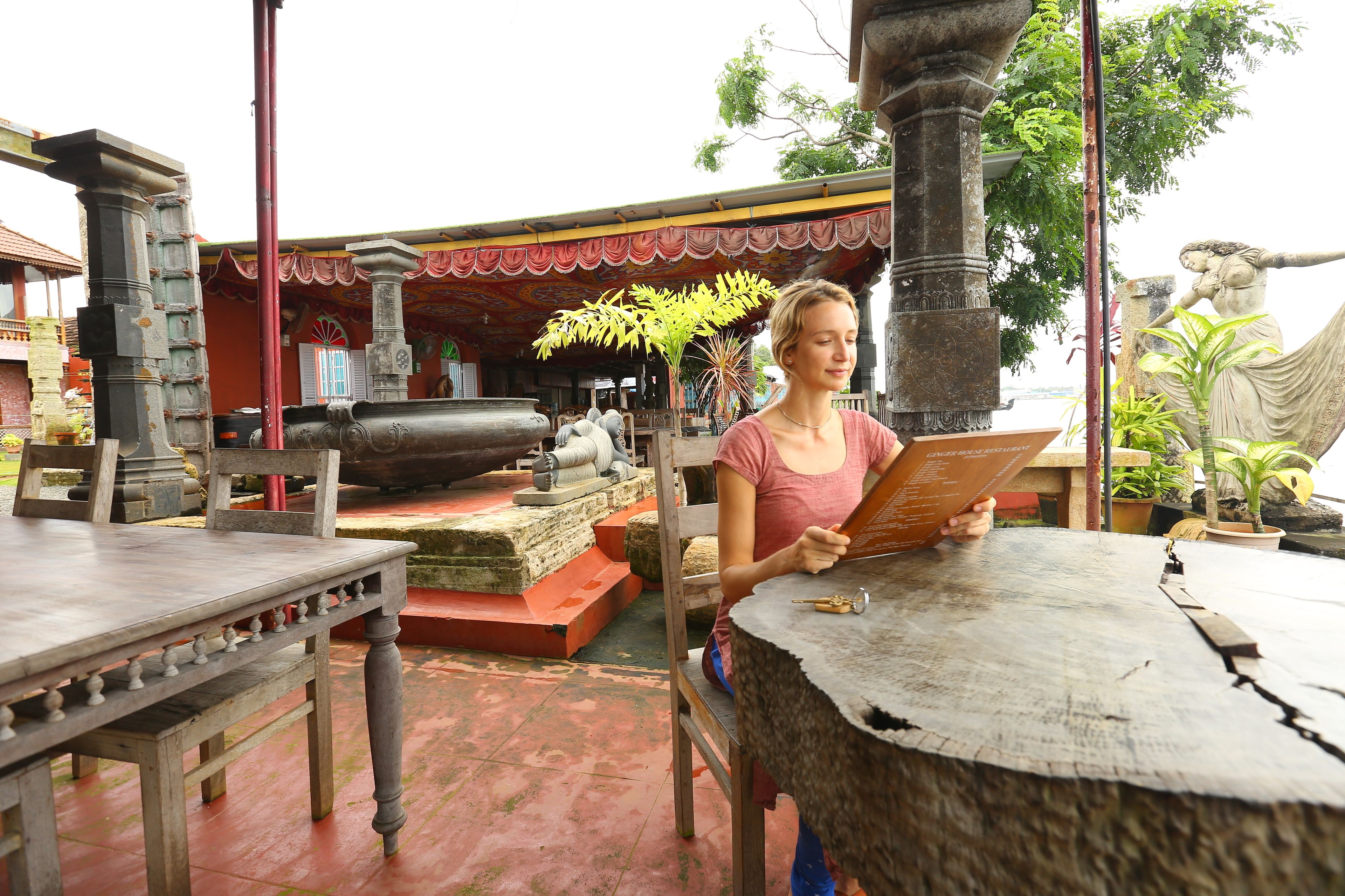 A person sitting at a wooden table outdoors, reading a book.