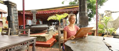 A person sitting at a wooden table outdoors, reading a book.